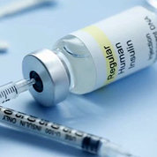 A bottle of insulin likes on a table with a syringe inserted.