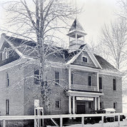 A black and white photograph of a two-story building constructed from locally-made bricks.