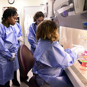 Five young people gathered at lab research hooded bench to observe demonstration.