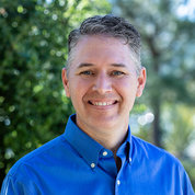 Dr. Shane Crotty smiling, in blue shirt, with trees behind him