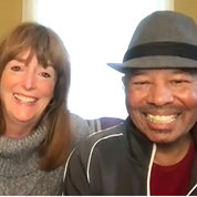 A screenshot of Burcombe and Harris sitting together on a couch, both smiling