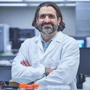 Dr. Adam Resnick in white lab coat, arms folded, standing in a lab